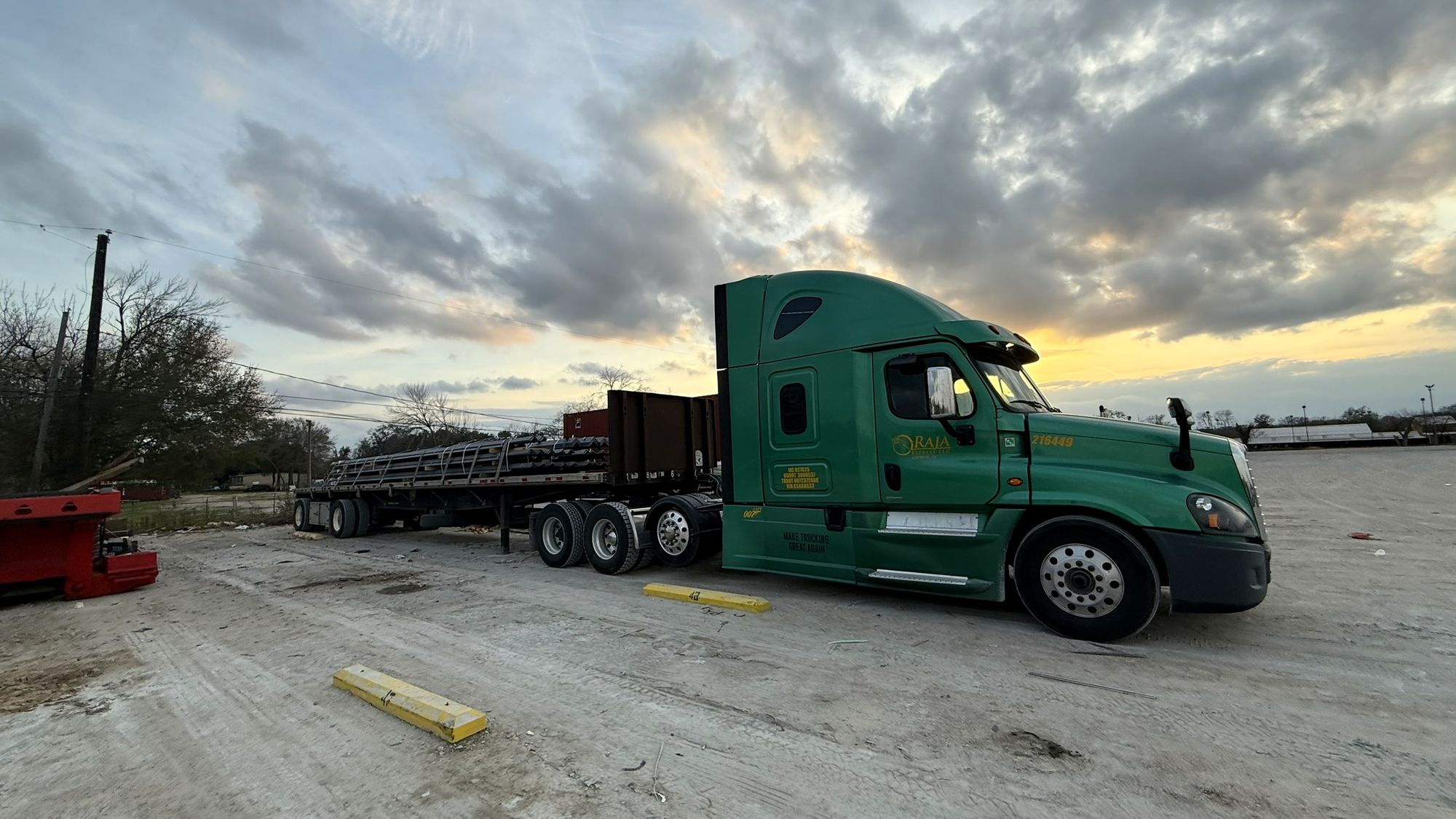 Green Raja Express truck with a strapped steel load on a flatbed at sundown